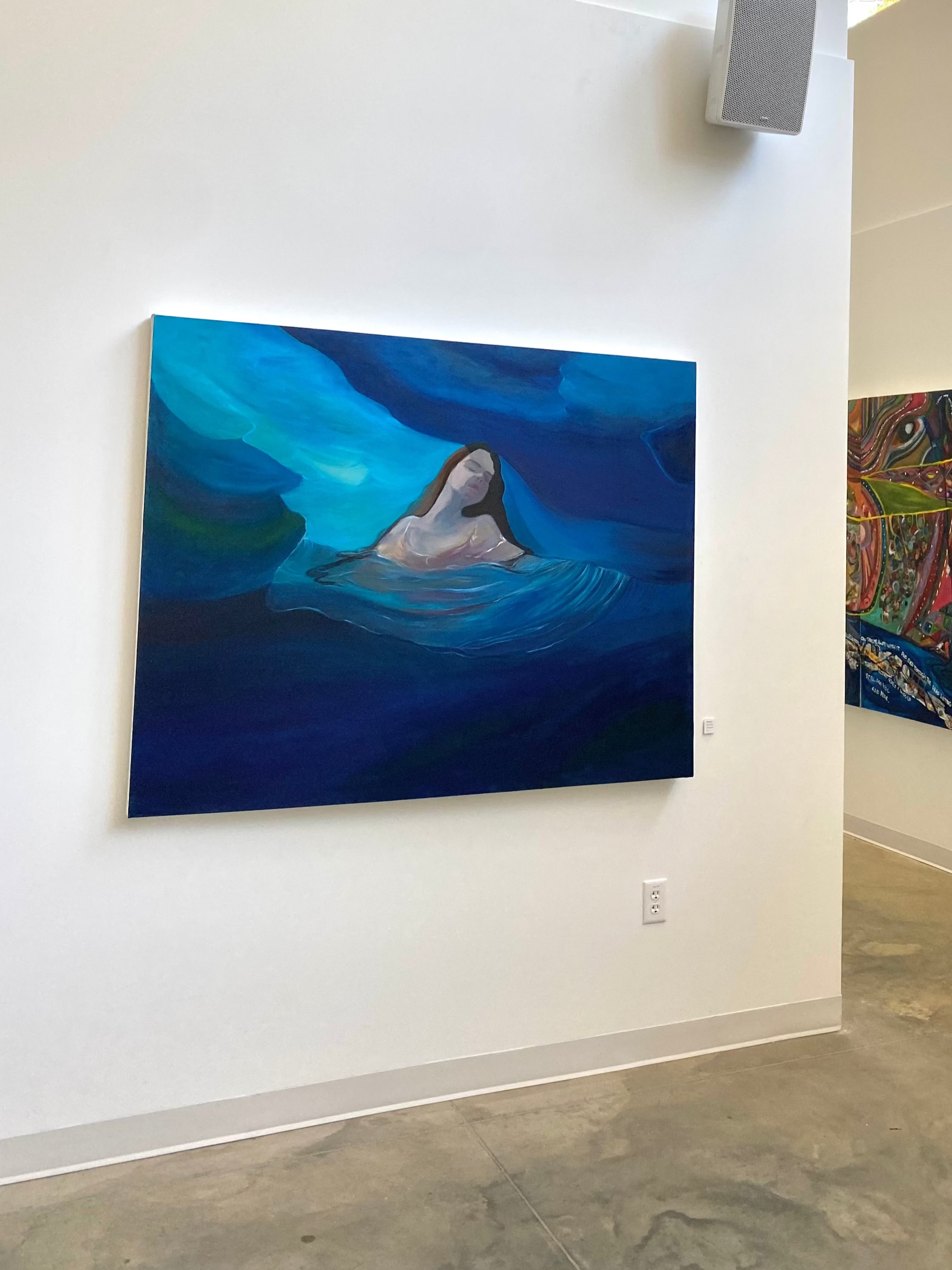Art gallery with two paintings on white walls, one blue and one multicolored.